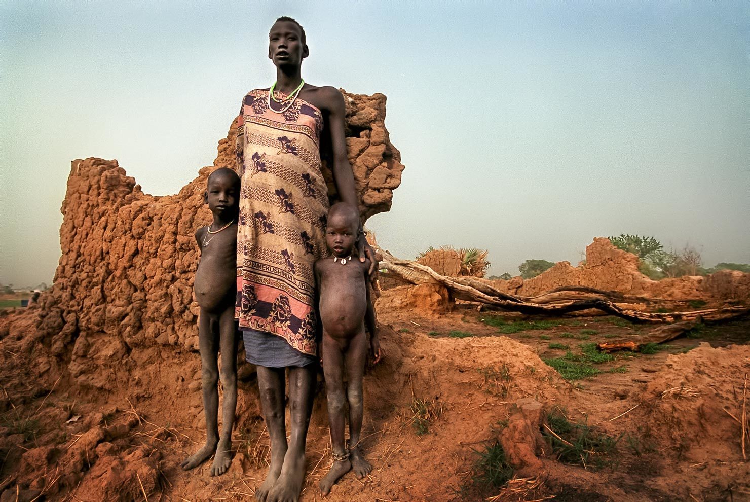 Sudanese mother & children with their home which was destroyed by war