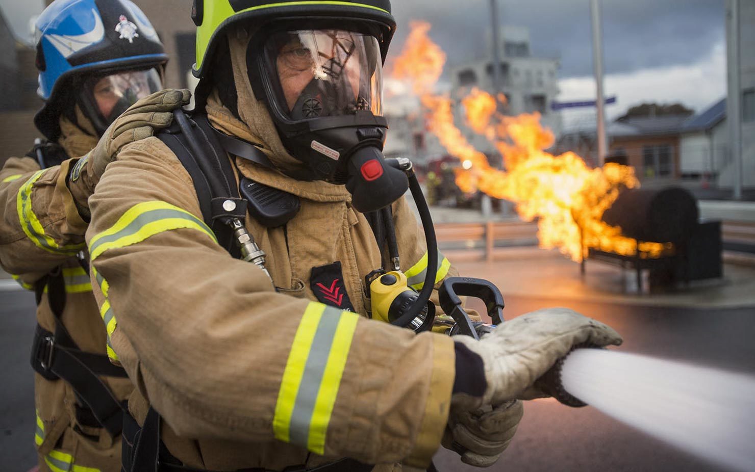 Firefighters spray water with fire behind them